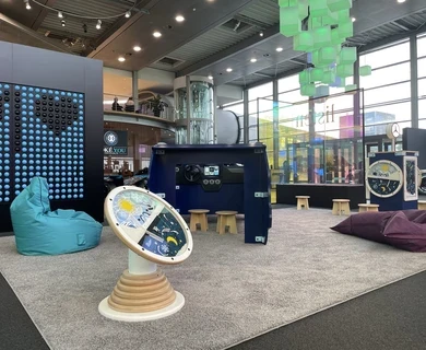 Kinderhoek in Mercedes-Benz Kundencenter met diverse speelobjecten, waaronder een blauw dashboard-speelmeubel, interactieve wandspellen, grote turquoise en paarse zitzakken en kleurrijke verlichting in een moderne showroomomgeving.