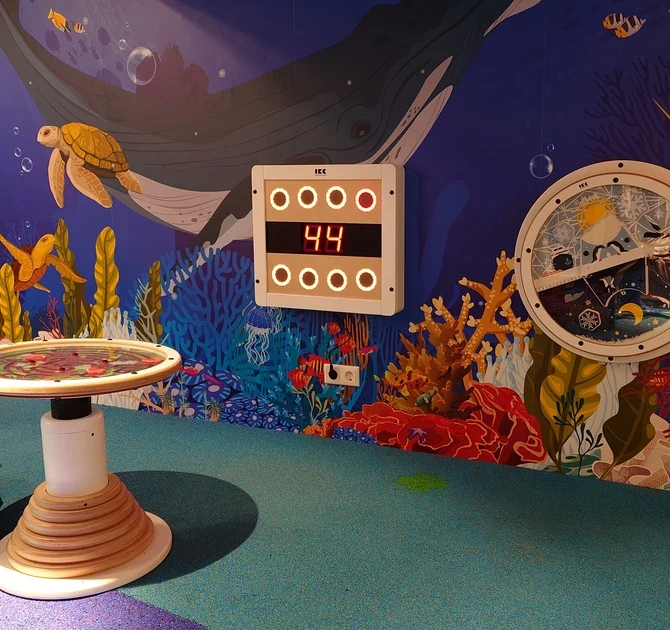 Kinderhoek in oceaanthema met digitale wandspellen, speeltafel, kleurrijke onderwaterillustraties en zachte zitzakken, ontworpen door IKC in een winkelcentrum.