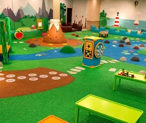 Large indoor playground with nature-themed EPDM flooring, play huts, interactive elements and a colorful landscape for children